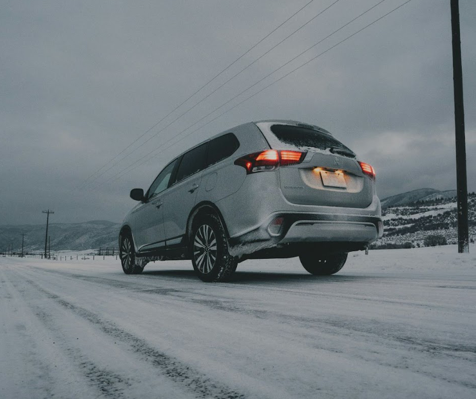 A low-angle of a silver SUV driving on an icy road in winter.