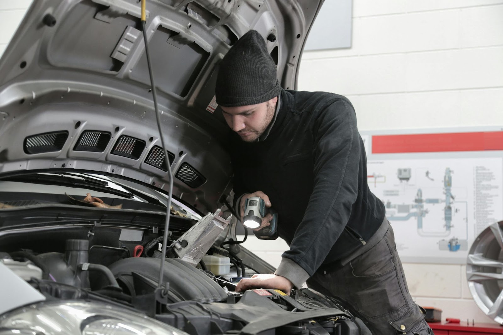 A car mechanic inspects a car engine with a flashlight.