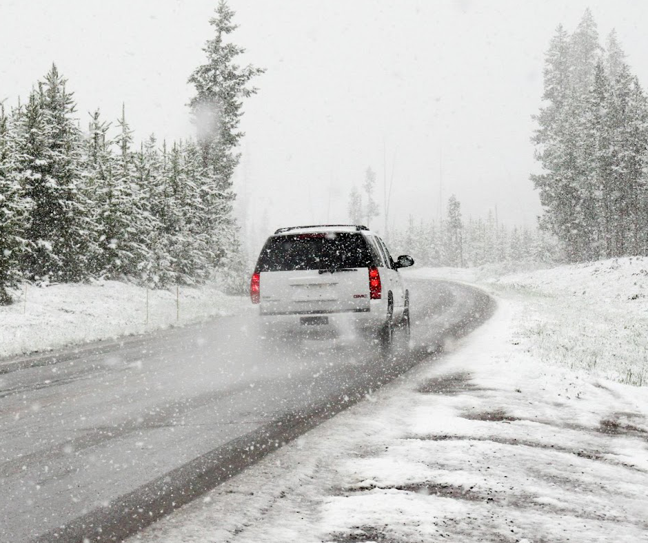 A white SUV driving along an icy road in heavy snowfall.