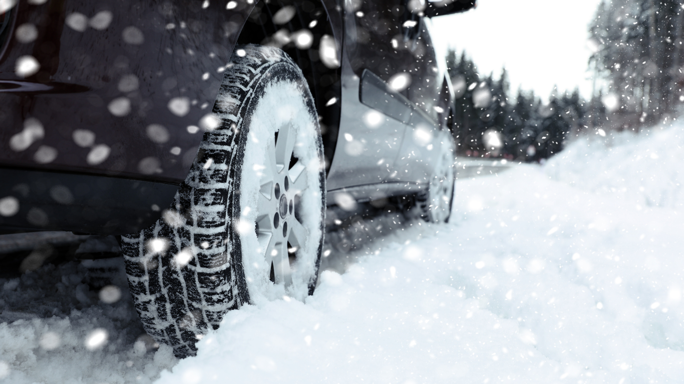 Vehicle equipped with winter tires driving through a snow-covered road.